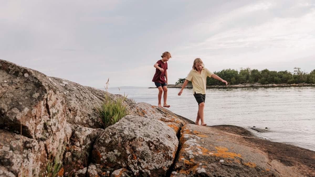 Två barn leker på klippor vid havet i Blekinge skärgård, Sverige, under en lugn sommarkväll. Aktiv utomhuslek och familjevänlig naturupplevelse vid kustnära miljö.