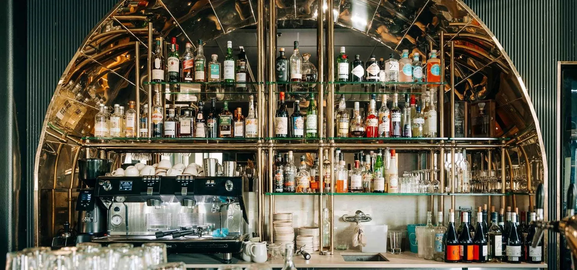 Elegant bar med glänsande guldinredning, hyllor fyllda med spritflaskor och en kaffemaskin i förgrunden, som skapar en lyxig atmosfär för en festlig nyårshelg i Blekinge.